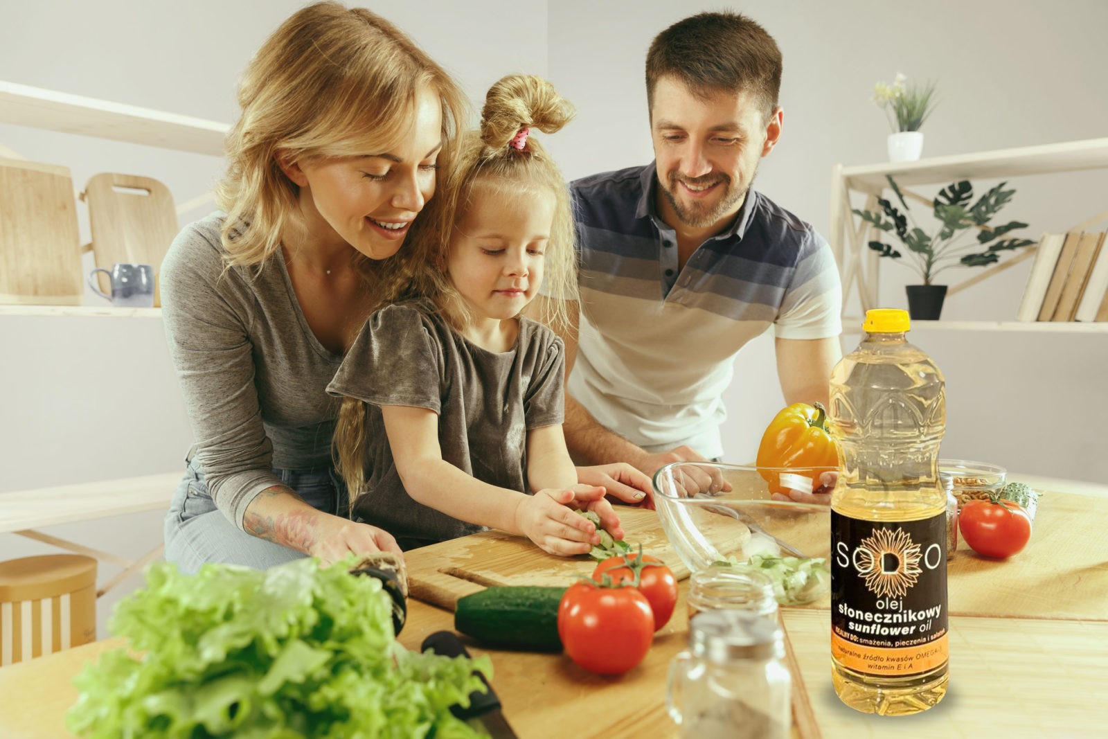 Cute little girl and her beautiful parents are cutting vegetables and smiling while making salad in kitchen at home. Family lifestyle concept